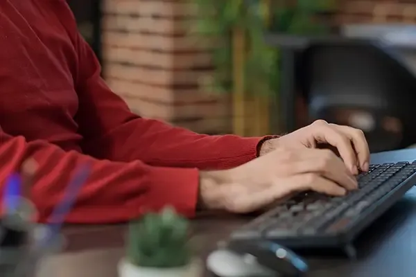 Person with red shirt typing on computer keyboard