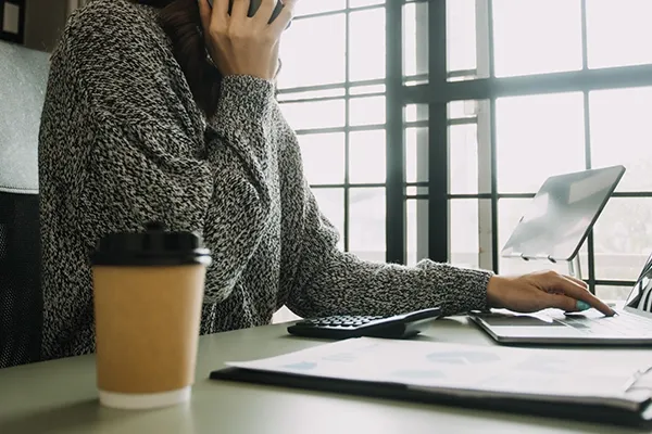 Person holding phone to right ear with coffee and laptop on desk