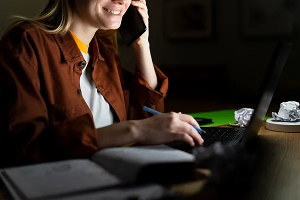 Woman holding phone up to left ear while typing on laptop
