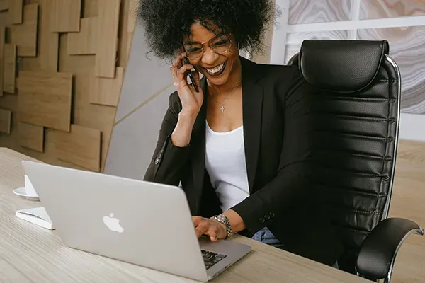 Woman smiling while on phone and typing on laptop