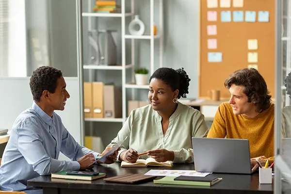 Three people sitting down around a table while talking with a laptop