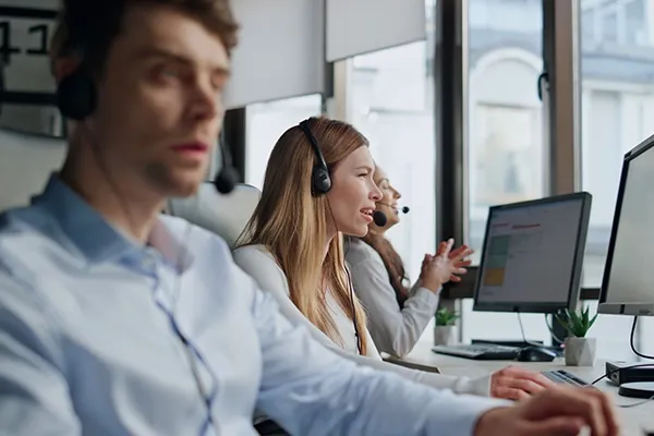 People talking with headsets on while looking at computer monitors