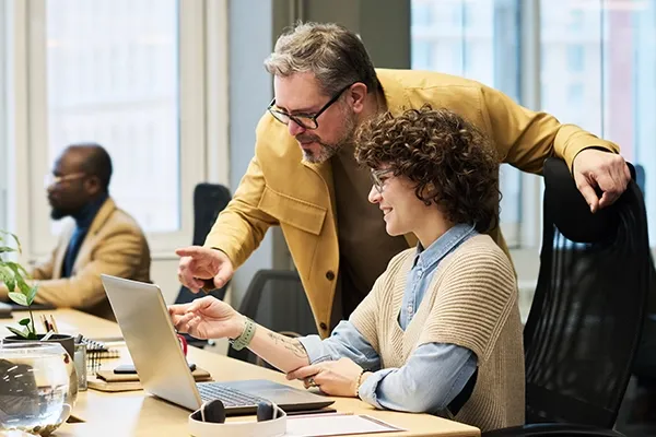 Man with glasses looking over woman on laptop
