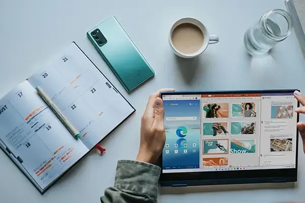 Person using Windows tablet with mobile phone and mug on desk