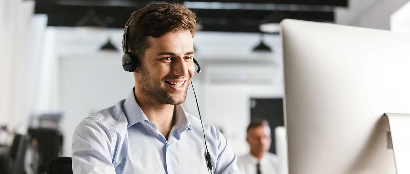 Man smiling with headset on while typing on computer