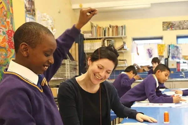 Boy holding hand in the air next to female teacher