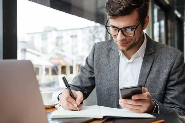 Man writing in a notebook copying from a mobile phone