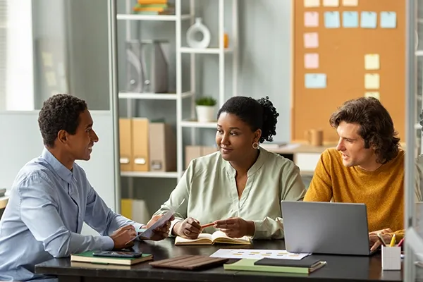 Three people sitting down around a table while talking with a laptop