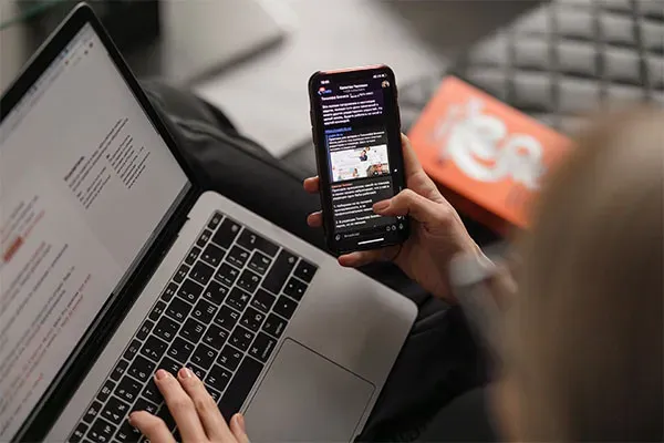 Person scrolling on phone while typing on laptop